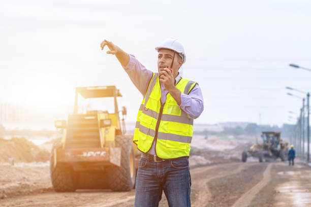 Engineer working on construction site, machine for road work background, Civil Engineers control and inspection with walkie-talkie, Soil and road work.